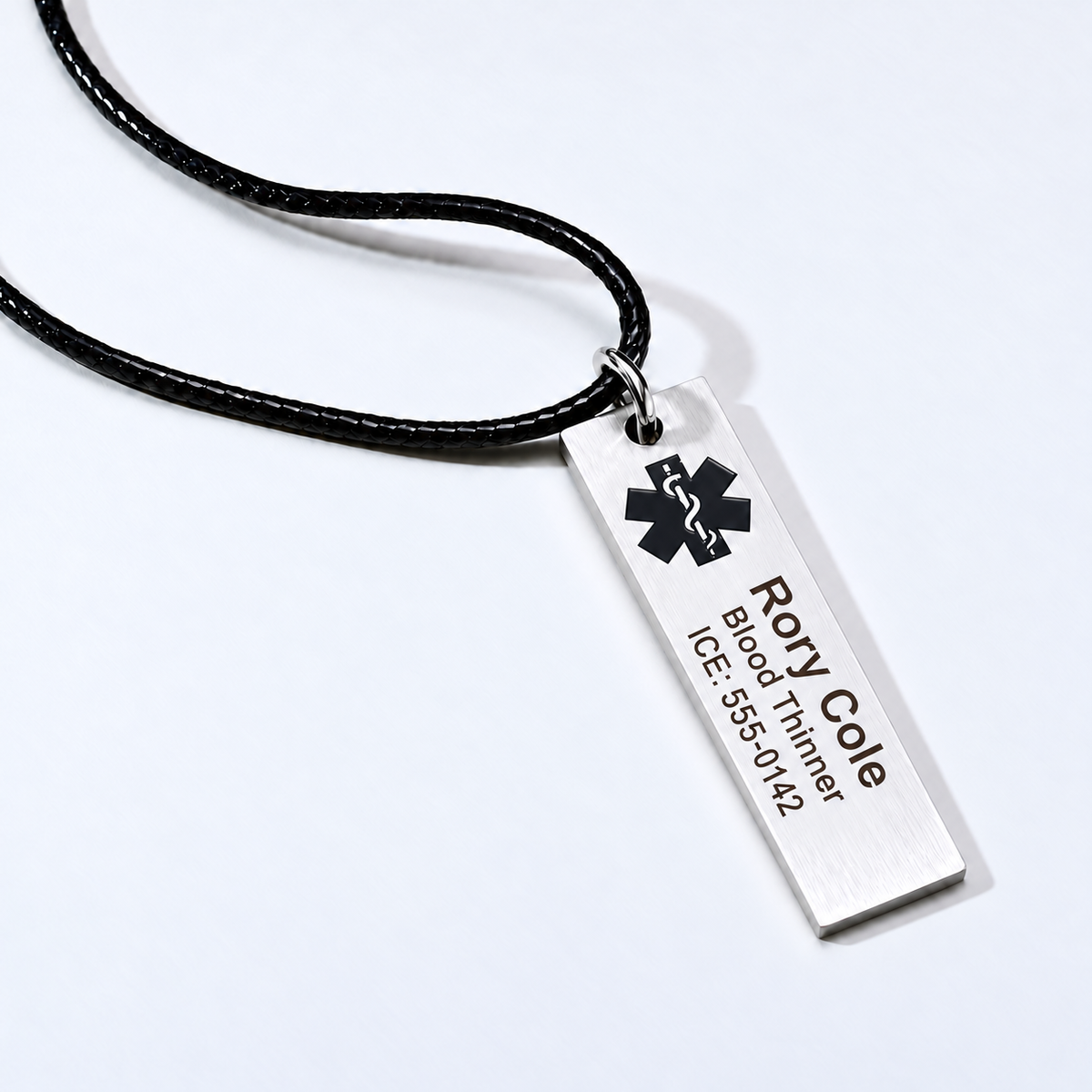 Silver medical ID bar pendant with centered lengthwise sample engraving and a larger name, on a black cord.